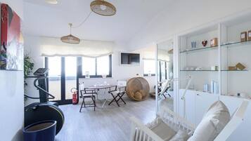 Ein modernes Wohnzimmer mit einem weißen Babybett, Trainingsgeräten und einem Essbereich mit rundem Tisch und Stühlen.