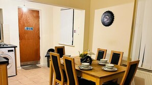 Un comedor con mesa y sillas de madera, una lavadora y una puerta con señal de salida de incendios.