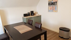 Ett litet kök med en kaffebryggare, vattenkokare och brödrost på bänkskivan. En papperskorg syns till höger.