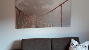 En grå soffa med en vit kudde och en stor, abstrakt tavla som föreställer en bro, hängd på väggen.