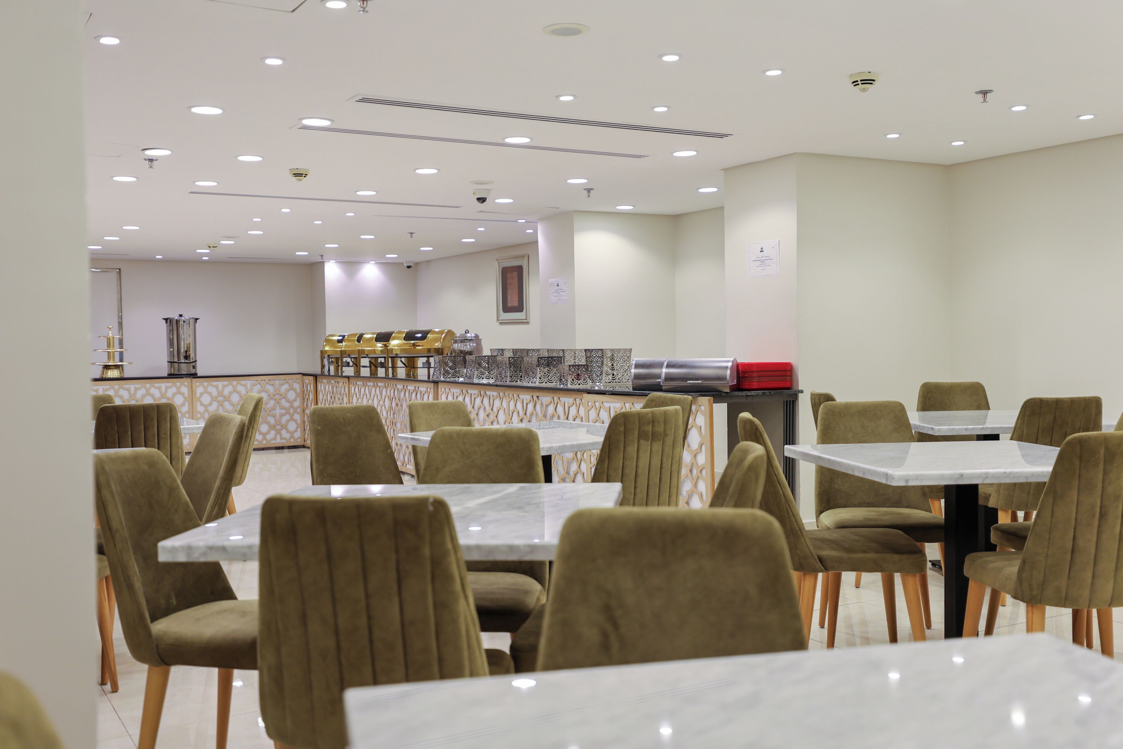 Restaurante com mesas de mármore e cadeiras estofadas, iluminação embutida no teto e um painel decorativo.