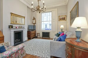 Cozy living room with a fireplace, TV, and comfortable sofa, offering a view of the outside through a large window.