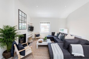 Ein modernes Wohnzimmer mit grauem Sofa, Couchtisch, Fernseher und einer großen Topfpflanze.