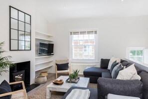 Ein modernes Wohnzimmer mit Kamin, Fernseher, einer Couch und einem großen Fenster.