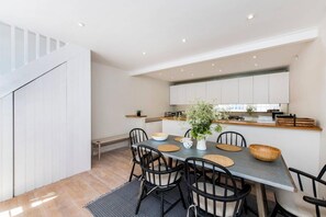 Una cocina moderna con armarios blancos, una mesa de comedor con sillas negras y una escalera que conduce a un nivel superior.