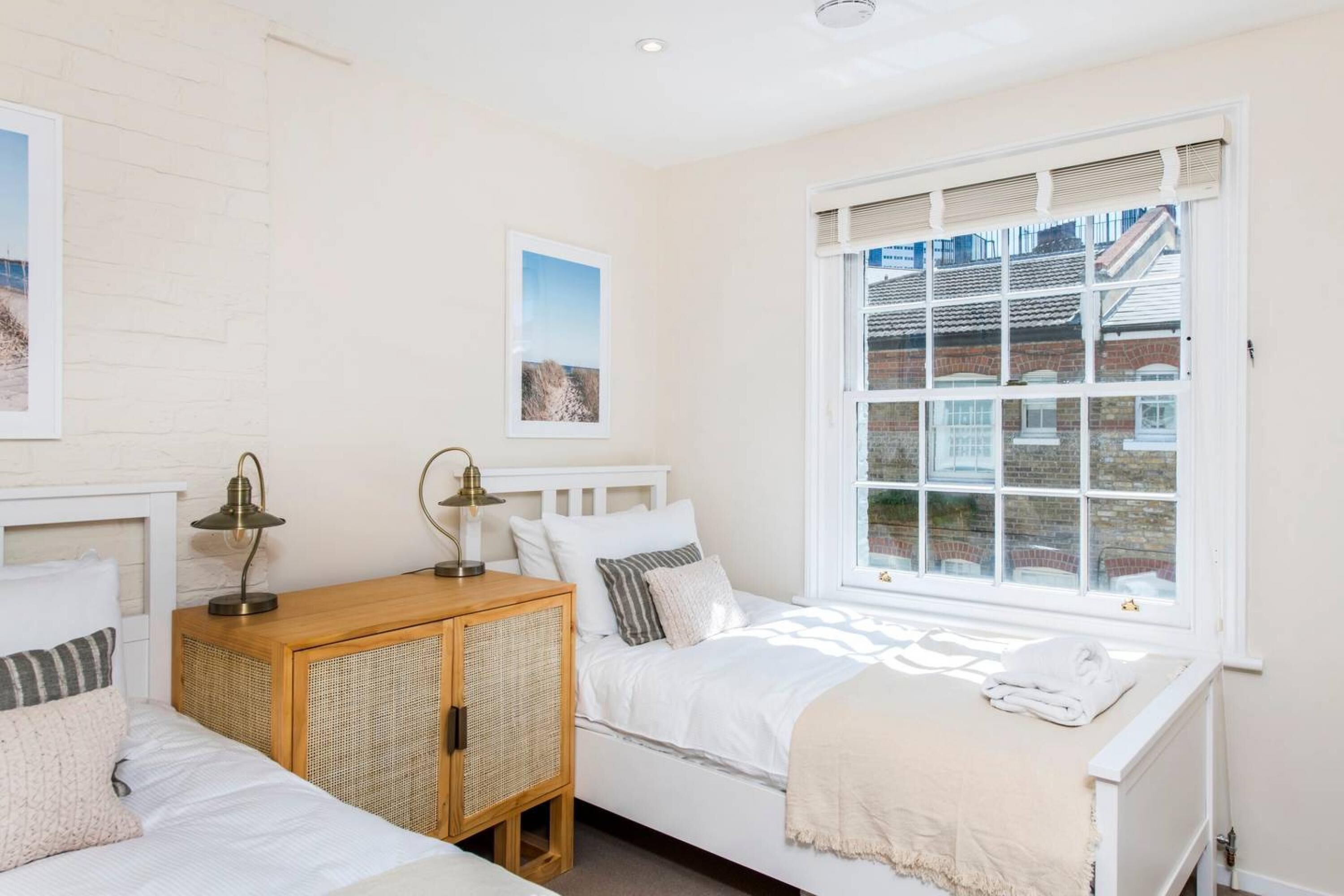 Une chambre avec deux lits, une armoire en bois et une grande fenêtre donnant sur des immeubles.