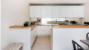 A modern kitchen with white cabinets, a wooden countertop, and a central island. - Divine 3-bed Mews House Battersea (London)