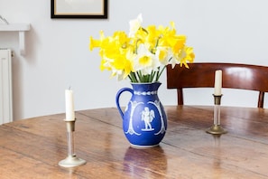 A blue ceramic pitcher with a white decorative figure, filled with yellow and white daffodils, placed on a wooden table.