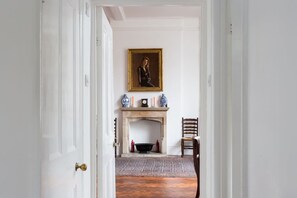 A hallway with a white door, a fireplace with a rug, and a framed portrait above it. - Artistic 1bed Flat (London)