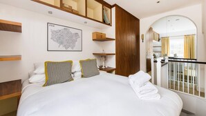 A hotel room with a large bed, wooden headboard, a map on the wall, a small table with a lamp, and a balcony with curtains.