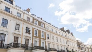 A row of traditional white buildings with multiple stories, featuring balconies with black railings and a clear blue sky with clouds.