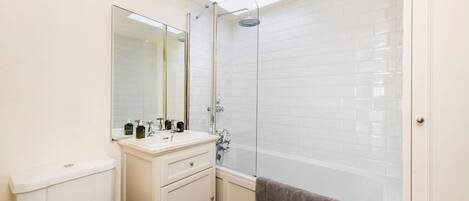 A bathroom with a toilet, sink, mirror, and shower.