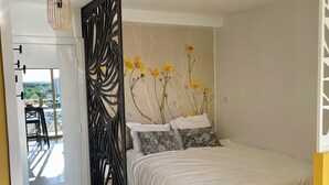 Een slaapkamer met een bed, een decoratief hoofdbord, uitzicht op de omgeving en een deur met een zwart decoratief paneel.