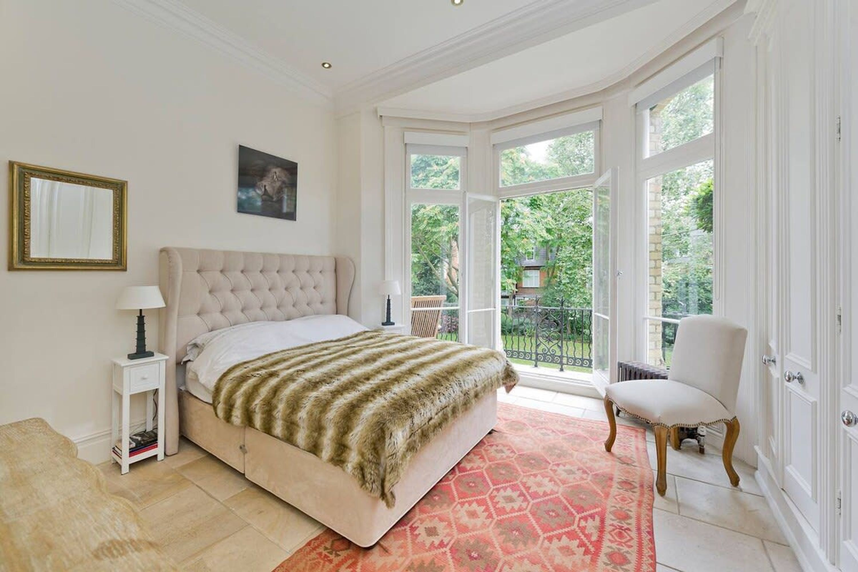 A bedroom with a large bed, a chair, a nightstand, and a window with a view of greenery.