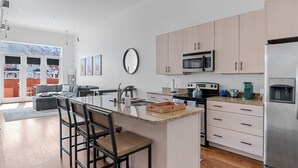 A modern kitchen with a central island, stainless steel appliances, and light wood cabinets. - Spacious Condo in Center of NULU with Free, Gated, Secure Parking and Entrance (Louisville)