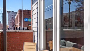 An outdoor patio with a wooden table and chairs, a brick wall, and a view of a building with an American flag. - Spacious Condo in Center of NULU with Free, Gated, Secure Parking and Entrance (Louisville)