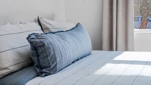 A bed with a striped bedspread and pillows, a window with curtains, and a view of a tree outside. - Spacious Condo in Center of NULU with Free, Gated, Secure Parking and Entrance (Louisville)