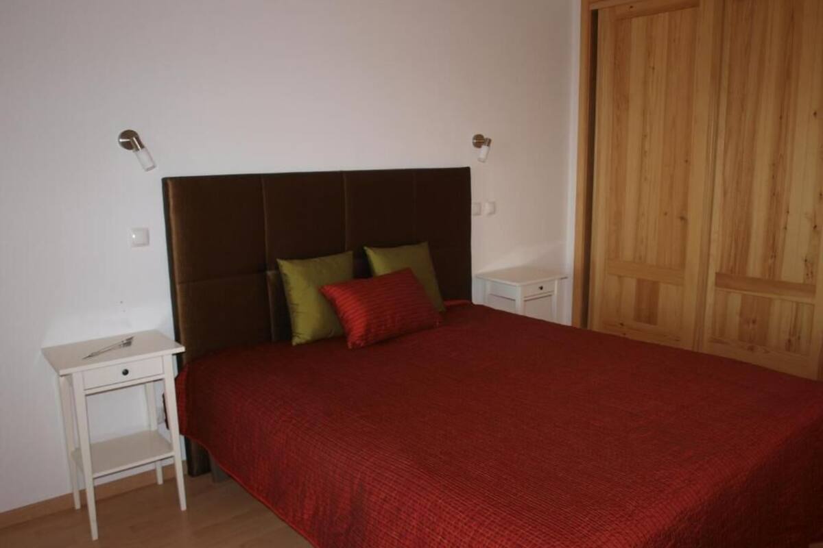 Une chambre avec un grand lit, une table de chevet, une armoire en bois et un mur blanc.