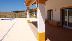 Un espacio al aire libre techado con piscina, vigas de madera y un edificio blanco y amarillo.