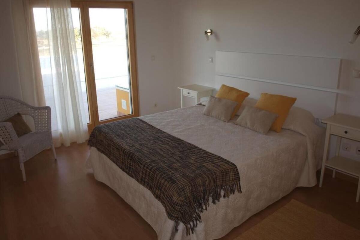 Une chambre à coucher avec un grand lit, une table de chevet, une chaise et une fenêtre avec des rideaux.