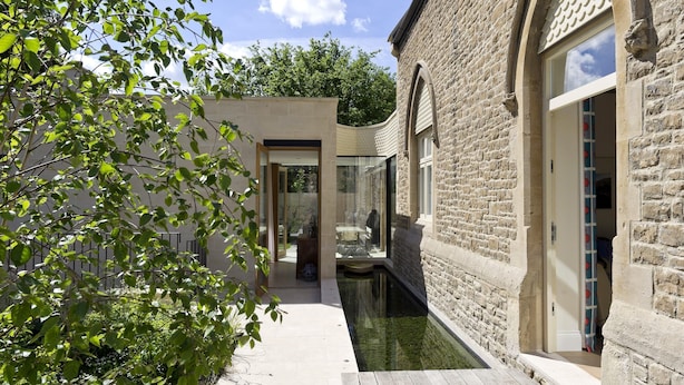 A narrow courtyard with a water feature, stone walls, and a glass door leading to a room. - Stunning 5 bed Fulham Home w Indoor Pool Sauna and Private Garden (London)