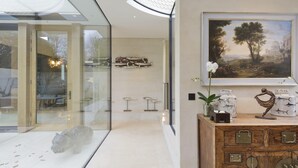 A modern interior with a glass door leading to a dining area, a wooden cabinet with decorative items, and a framed landscape painting on the wall. - Stunning 5 bed Fulham Home w Indoor Pool Sauna and Private Garden (London)