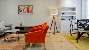 A modern living room with a sofa, orange armchairs, a coffee table, a floor lamp, and a bookshelf. - Sweet Marble Arch 2 Bedroom Mews House (London)