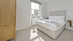 Quarto com cama, janela com vista, radiador e guarda-roupa de madeira.
