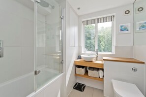 Une salle de bain moderne avec une douche en verre, un lavabo blanc et une fenêtre donnant sur la verdure à l’extérieur.