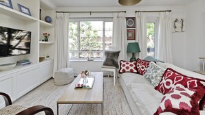 A living room with a sofa, a coffee table, a television, and a window with curtains. - Elegant 2 bed Flat Earls Court (London)