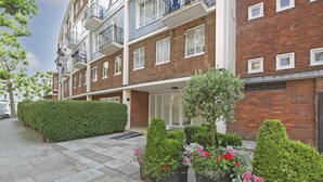 A multi-story residential building with balconies, a brick facade, and a well-maintained garden area with various plants and flowers. - Elegant 2 bed Flat Earls Court (London)