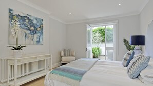 A bedroom with a large bed, a radiator, a painting, and a view of greenery outside. - Huge Kensington Garden Flat (London)