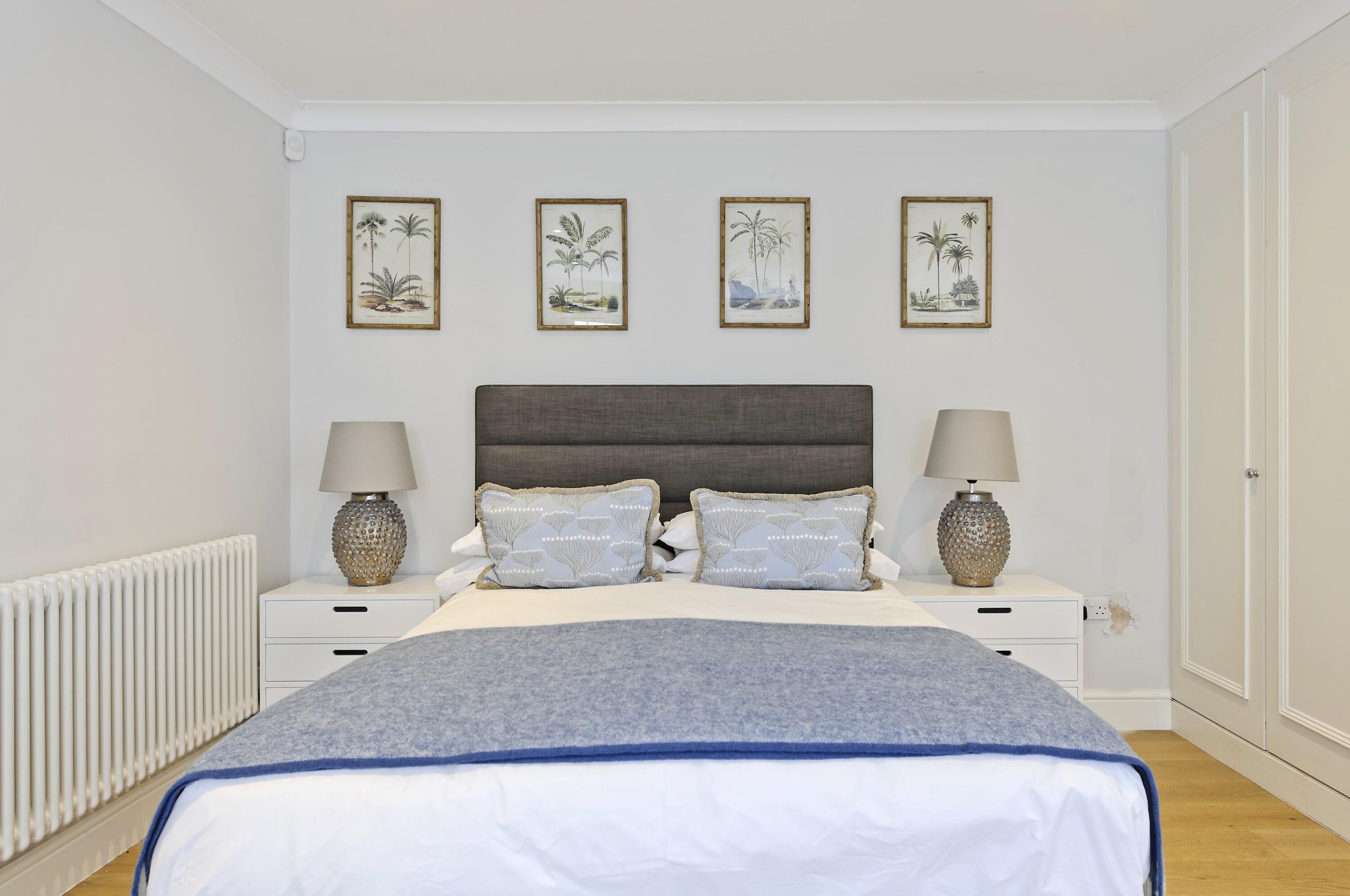 A bedroom with a bed, two bedside tables, and three framed pictures on the wall.