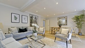 A modern living room with a grey sofa, a glass coffee table, and a dining area with a table and chairs. - Huge Kensington Garden Flat (London)