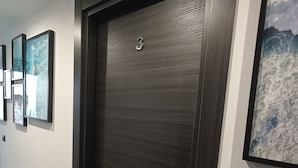 Een donkerhouten deur met daarboven het cijfer '3', een zilveren deurklink en een lichtschakelaar aan de muur.