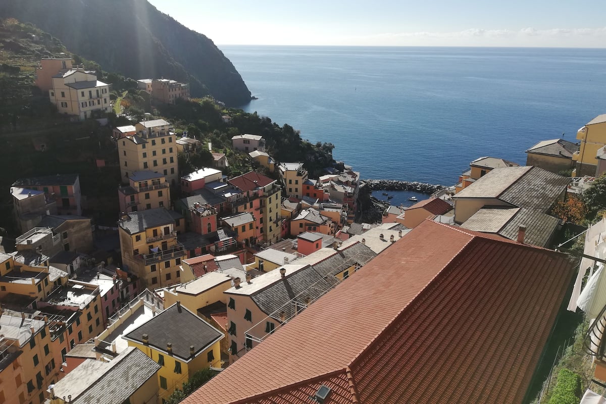 Ein Küstenort mit bunten Häusern, einer felsigen Hügelslope und Blick auf das Meer.