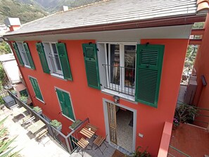 Un immeuble de deux étages avec des volets verts, un balcon agrémenté de meubles en bois et une vue sur les environs.