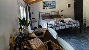 Een slaapkamer met een bed, een bureau met stoel, een raam, een schilderij aan de muur en een deur.