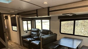 Ein kompaktes Wohnmobil-Interieur mit Essbereich, Sitzgelegenheiten und Fenstern, die Ausblicke ins Freie bieten.