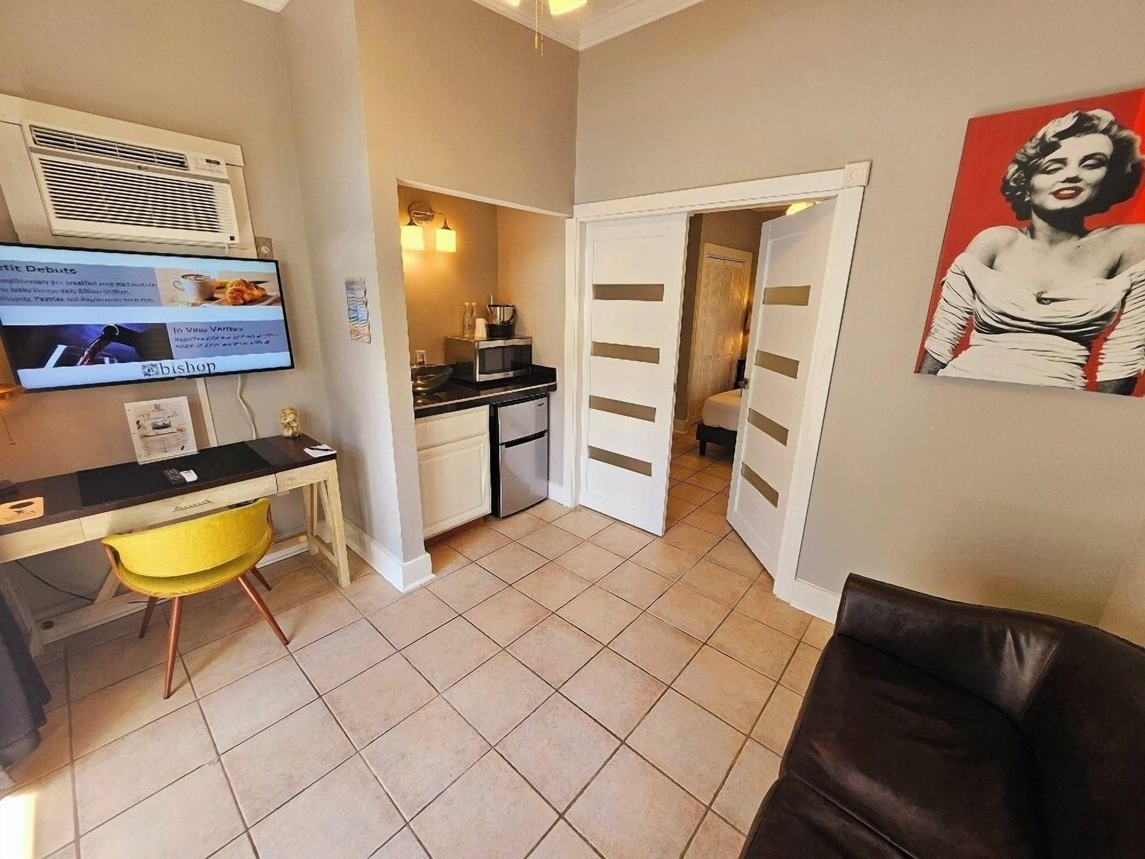 A compact living space with a kitchenette, a dining area with a yellow chair, and a black leather sofa.