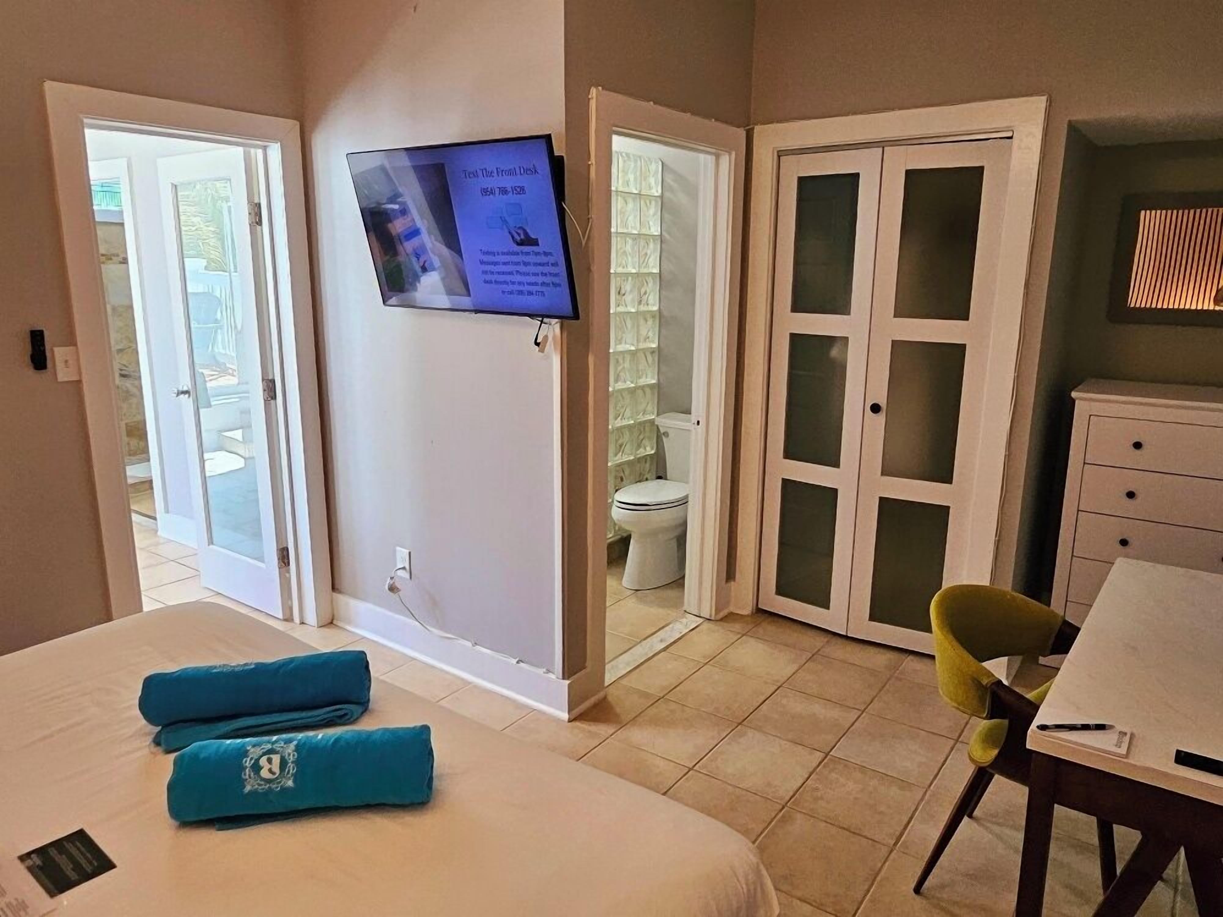 A hotel room with a bed, a desk, a chair, a TV mounted on the wall, and a bathroom visible through an open door.