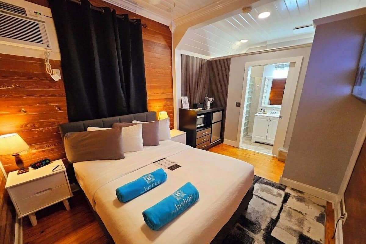 A hotel room with a bed, a nightstand, a desk, and a bathroom visible through an open door.