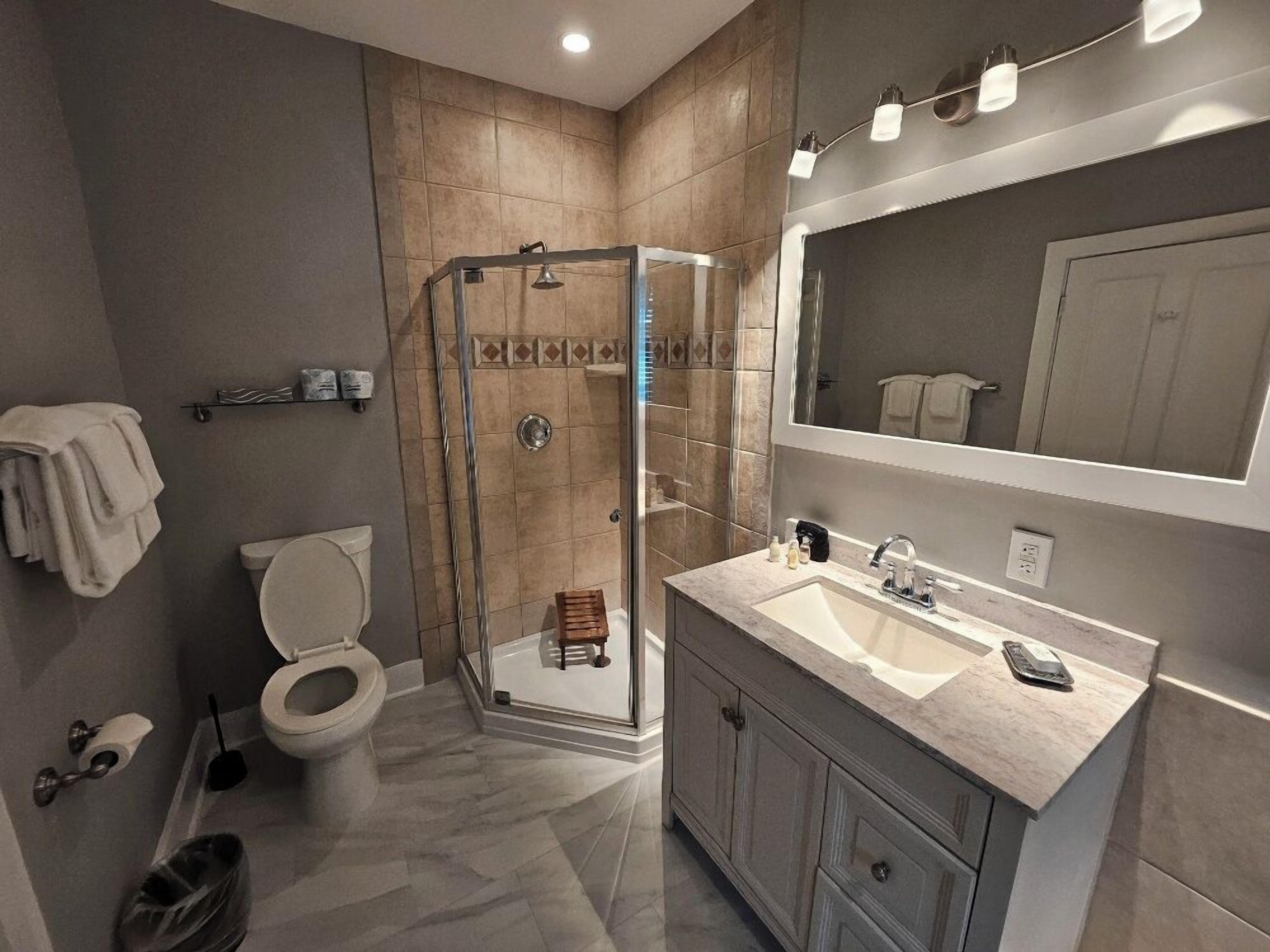 A modern bathroom with a glass-enclosed shower, a toilet, a sink with a mirror, and a towel rack.