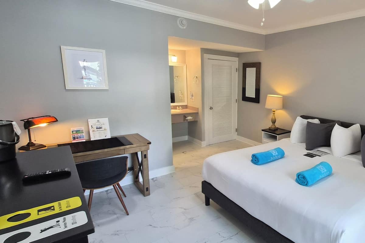 A hotel room with a bed, bedside tables, a desk, a chair, a lamp, and a mirror.