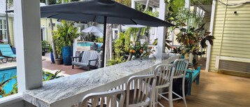 A covered outdoor seating area with a pool, chairs, and potted plants.