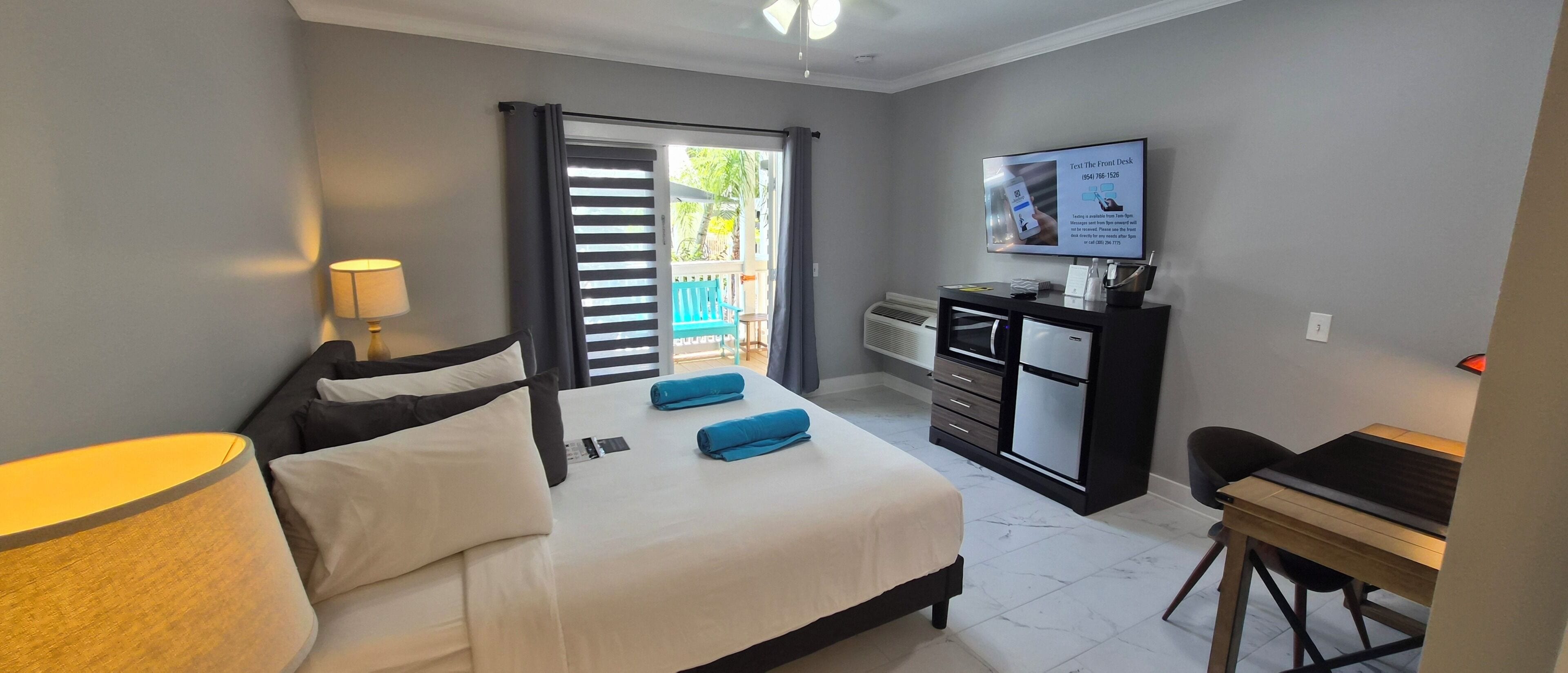 A hotel room with a bed, a desk, a television, and a balcony with a view.