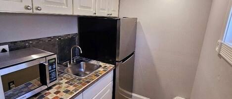 Una cocina compacta con armarios blancos, un refrigerador negro, un microondas y un salpicadero de azulejos.