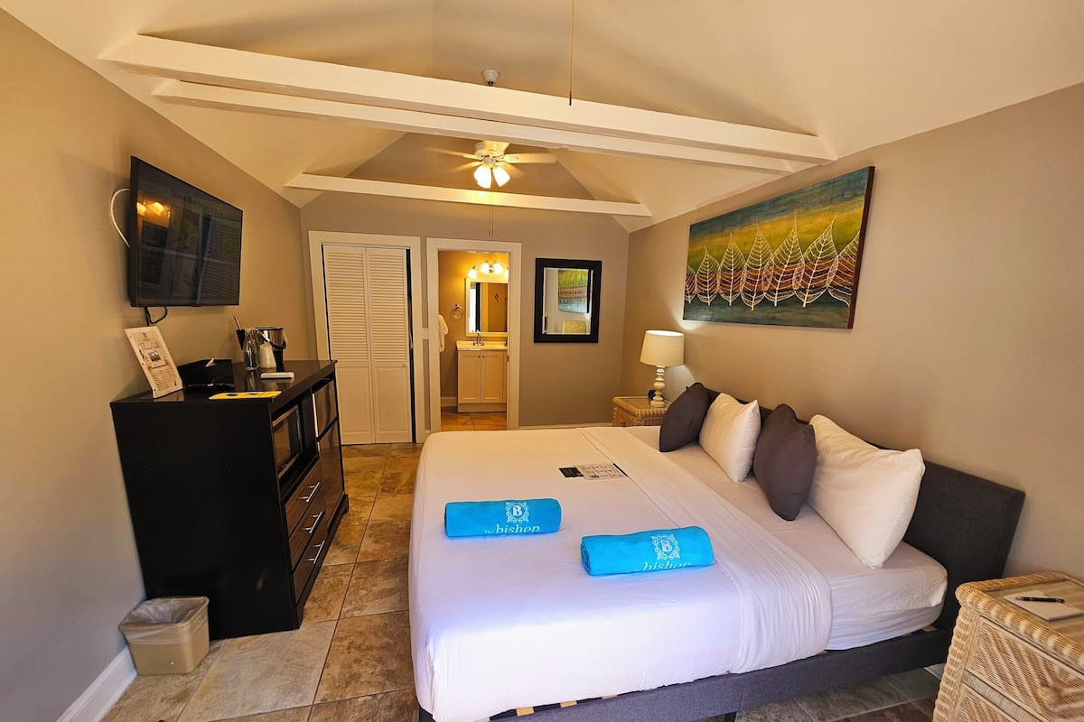 A hotel room with a bed, a desk, a wardrobe, a bathroom, and a painting on the wall.
