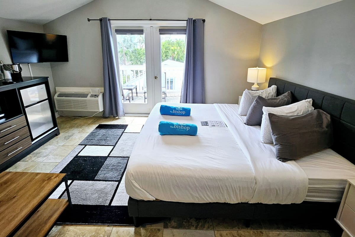 A hotel room with a bed, a desk, a television, and a view of the outdoors through a sliding door.