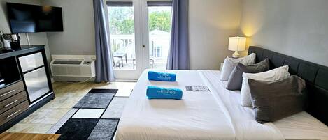 A hotel room with a bed, a desk, a television, and a view of the outdoors through a sliding door.